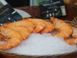 Fresh wild prawns displayed on ice in a market basket, ready for seafood lovers.